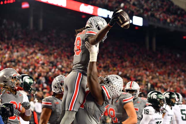 A football player wearing a gray uniform with red trim is lifted in the air by a teammate following a touchdown.